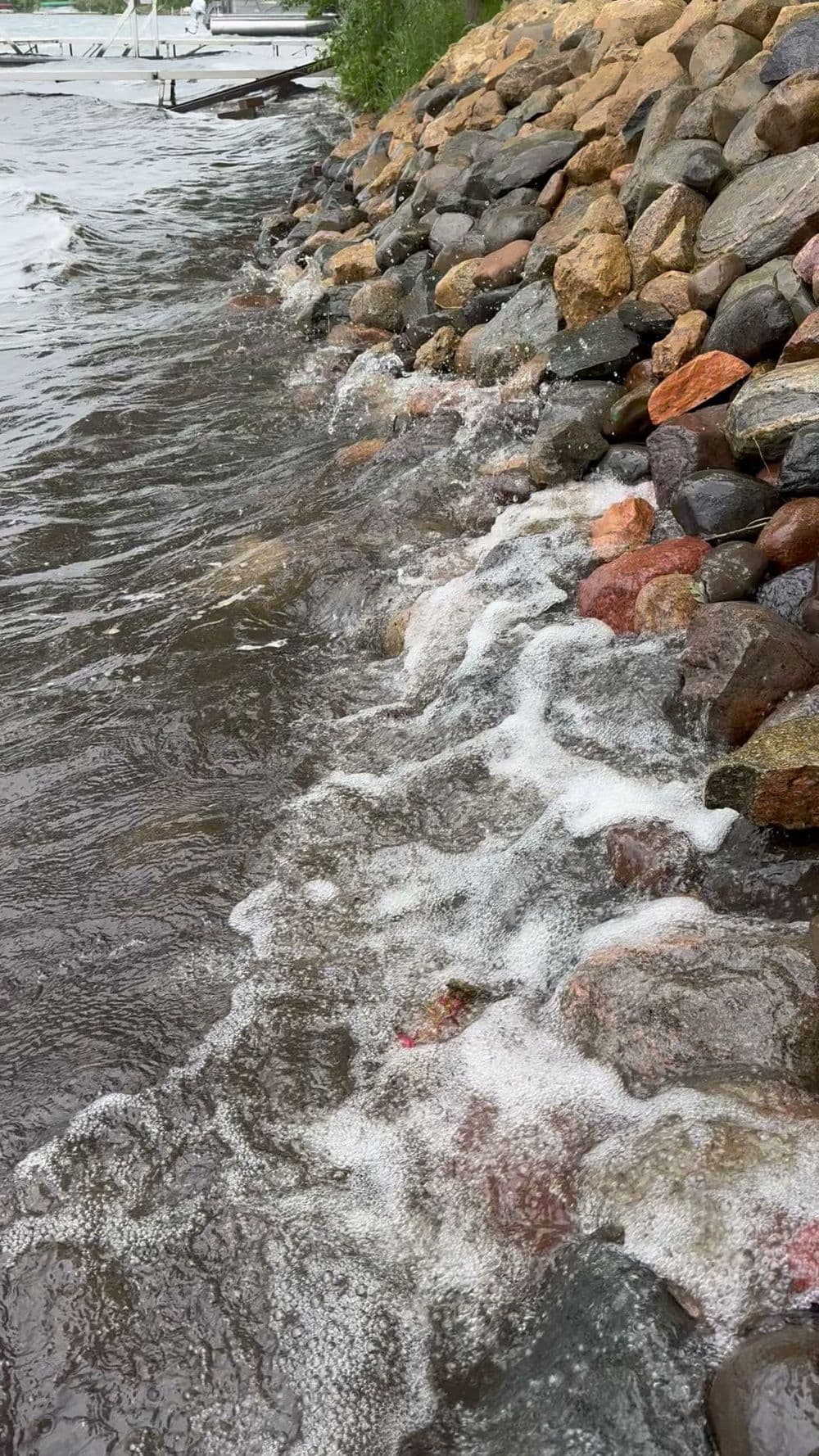 Rippling water over colorful stones along a lakeshore with gentle waves and foam.