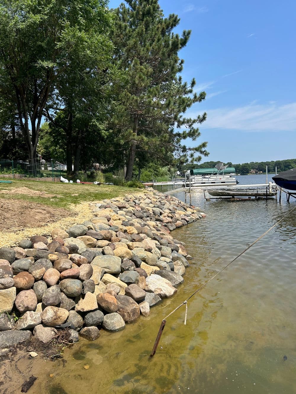 Lakeside scene with rocky shoreline, trees, and docks under a clear blue sky.