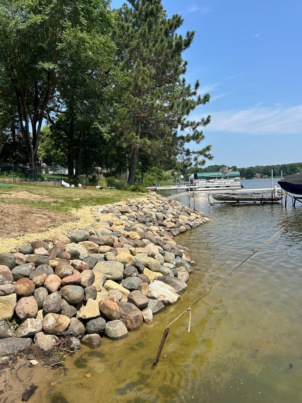 Stunning lakeside view with a rocky shoreline, trees, and boats on a calm summer day.
