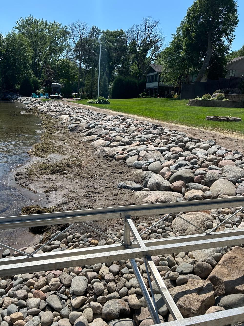 Rocky shoreline with a grassy area and trees in the background on a sunny day.