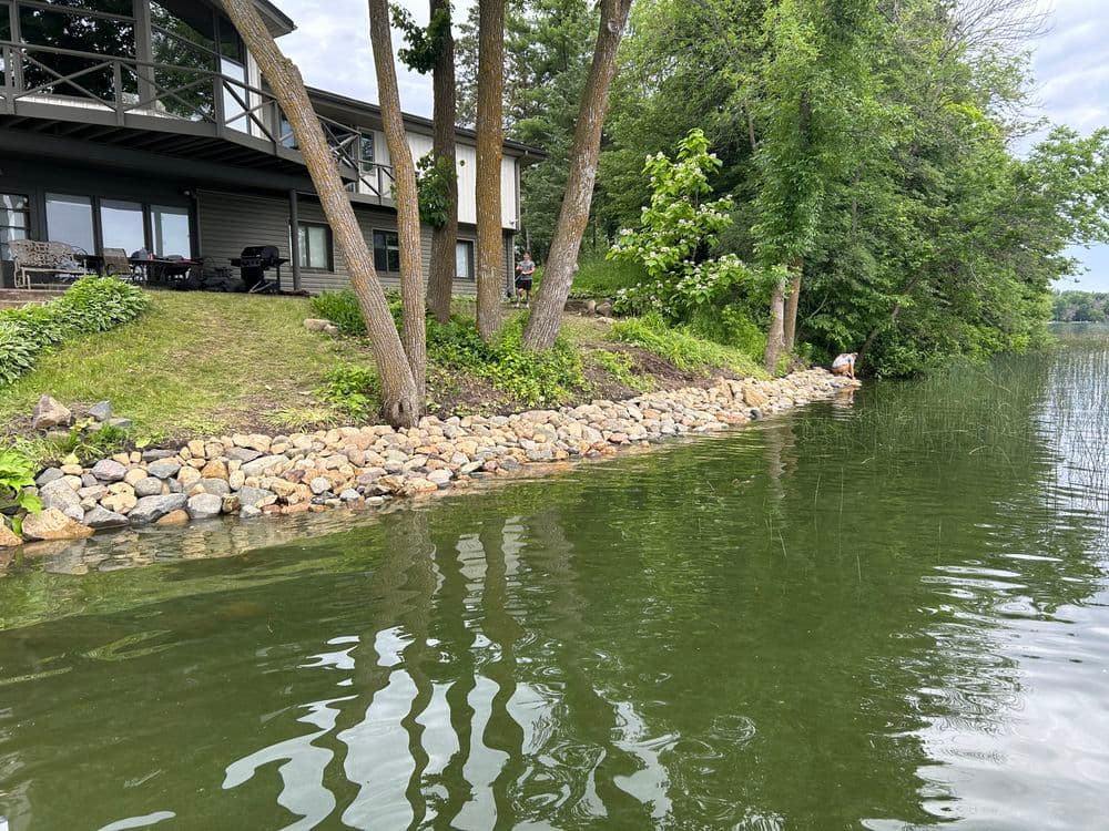Scenic lakeside view with rocky shoreline, trees, and a house. Peaceful water reflections.